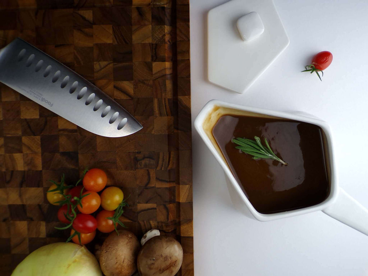 Insulated HeatTHAT! Gravy boat filled with hot gravy on a kitchen counter with fresh vegetables and a knife.