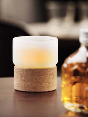 Double-walled Chill Glass with cork base, keeping beverages ice-cold without dilution, displayed next to a bottle on a wooden table.