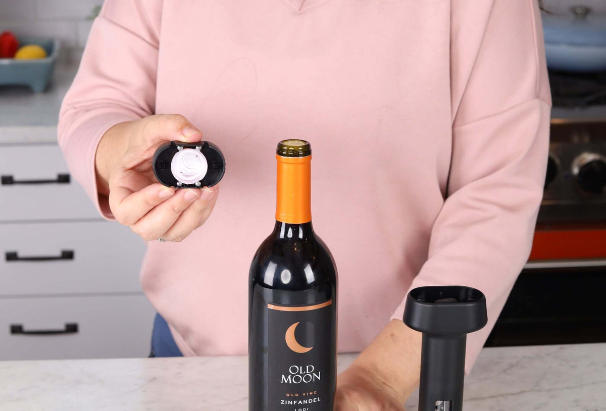Person using Corkie tool to open a bottle of red wine in a kitchen setting.