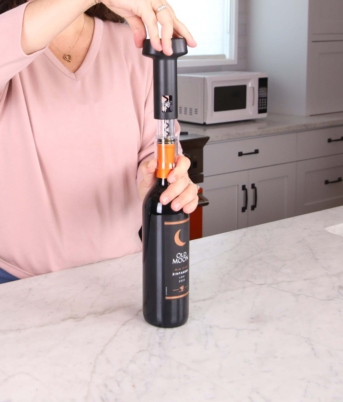 Woman using Corkie all-in-one corkscrew opener on wine bottle in a kitchen setting.