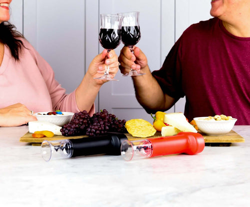 People toasting with wine glasses, showcasing Corkie corkscrew opener sets on a table with assorted cheeses and fruits.
