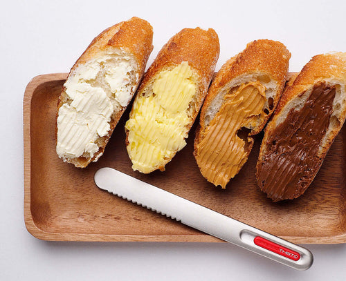 SpreadTHAT! butter knife with serrated edge spreading butter, cream cheese, peanut butter, and chocolate on bread slices.